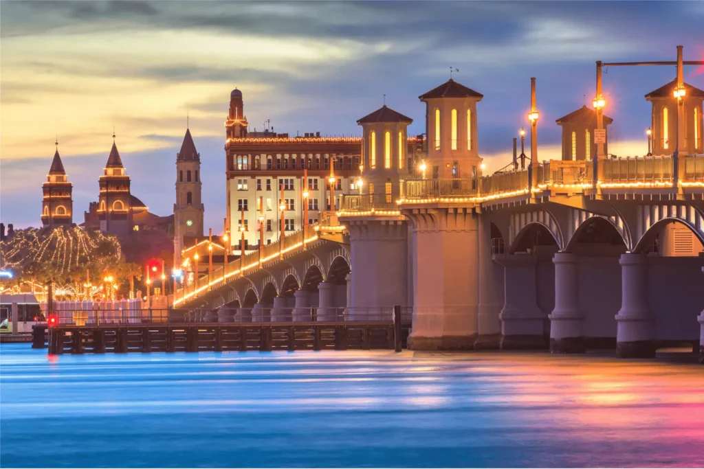 Bridge of Lions in St. Augustine, Florida, illuminated at dusk with historic buildings in the background.