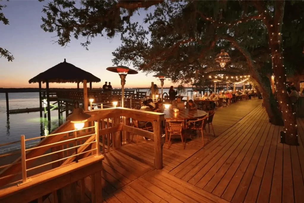 Waterfront restaurant deck with outdoor dining, string lights, and sunset views over the water.