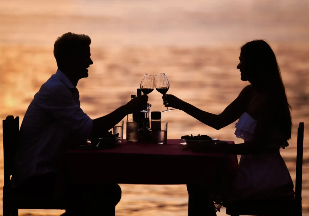 Couple toasting wine during a romantic waterfront dinner at sunset.