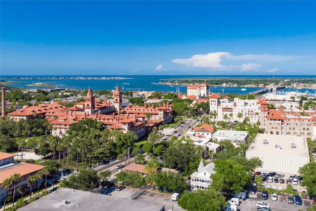Aerial view of historic St. Augustine, Florida, with the waterfront, marina, Bridge of Lions, and red-roofed buildings.