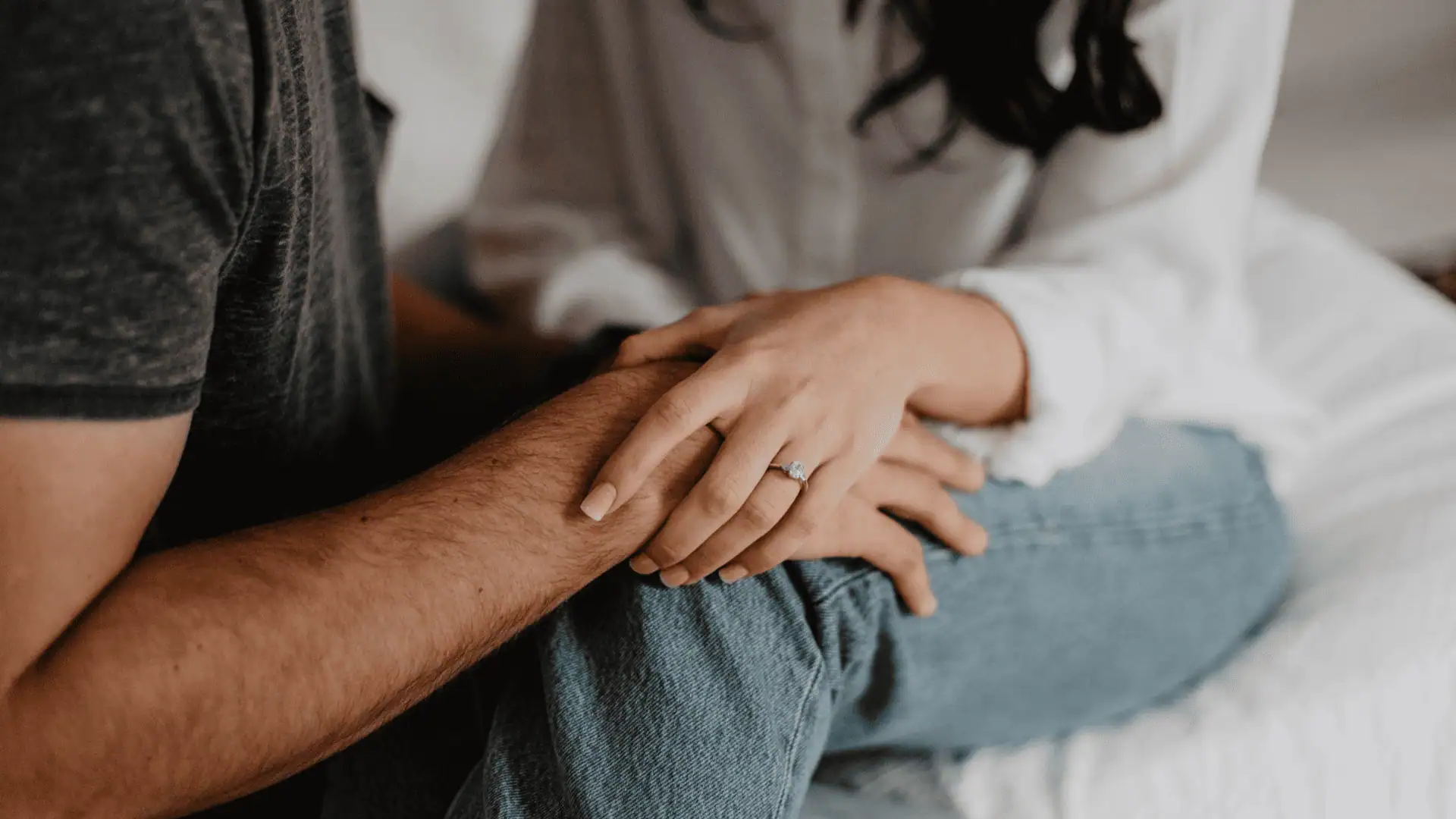 Couple sitting close together with one partner resting their hand on the other during a private relationship therapy moment.