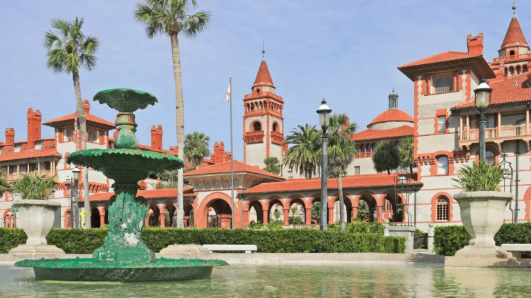 A weathered green fountain in front of the historic Lightner Museum architecture with palm trees in St. Augustine